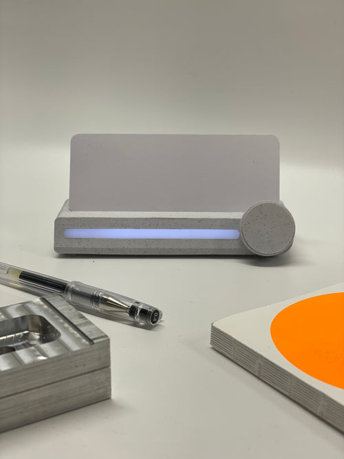 A gray Pomo Focus Timer device with a marble PLA 3D printed case, a digital display, and a knob on the right side, situated on a flat surface with a pen and orange object in the background.
